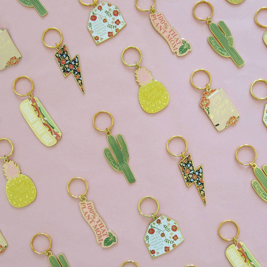 Variety of gold keychains laying flat including a hot dog, cactus, and more.