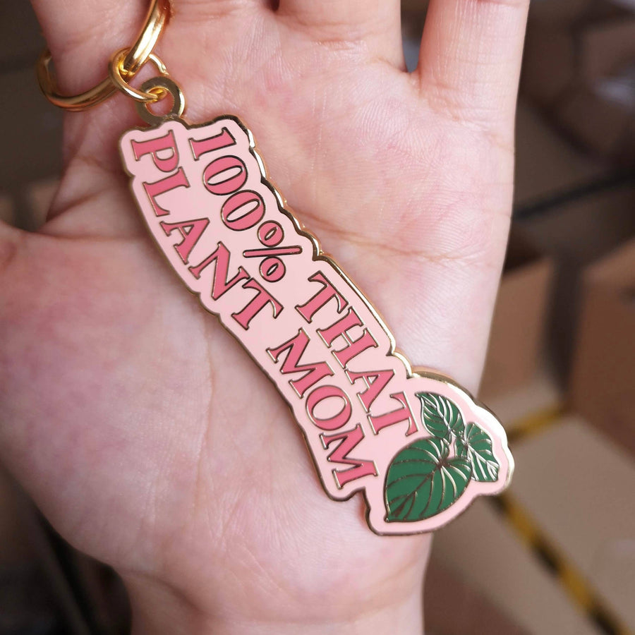 Pink keychain that reads 100% that plant mom with gloriosum plant
